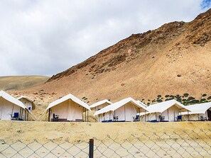 Une rangée de tentes blanches, séparée par une clôture en treillis métallique, avec une chaîne de montagnes en arrière-plan.