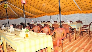 A tented dining area with multiple tables and chairs, each set with plates, cutlery, and condiments. - Tsomoriri Camp And Resort (Leh)