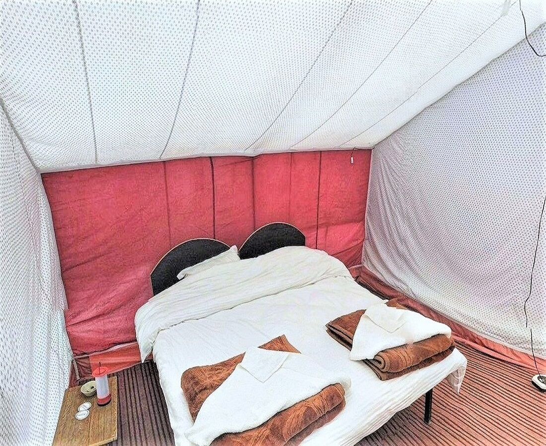 Een tentvormige kamer met een bed, kussens en een klein tafeltje met een kaars.