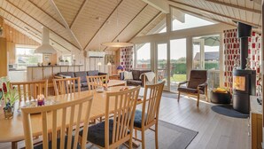A spacious, open-plan living area with a high ceiling and large windows, featuring a dining table, sofas, and a fireplace. - Gorgeous home in Sydals with sauna (Sydals)