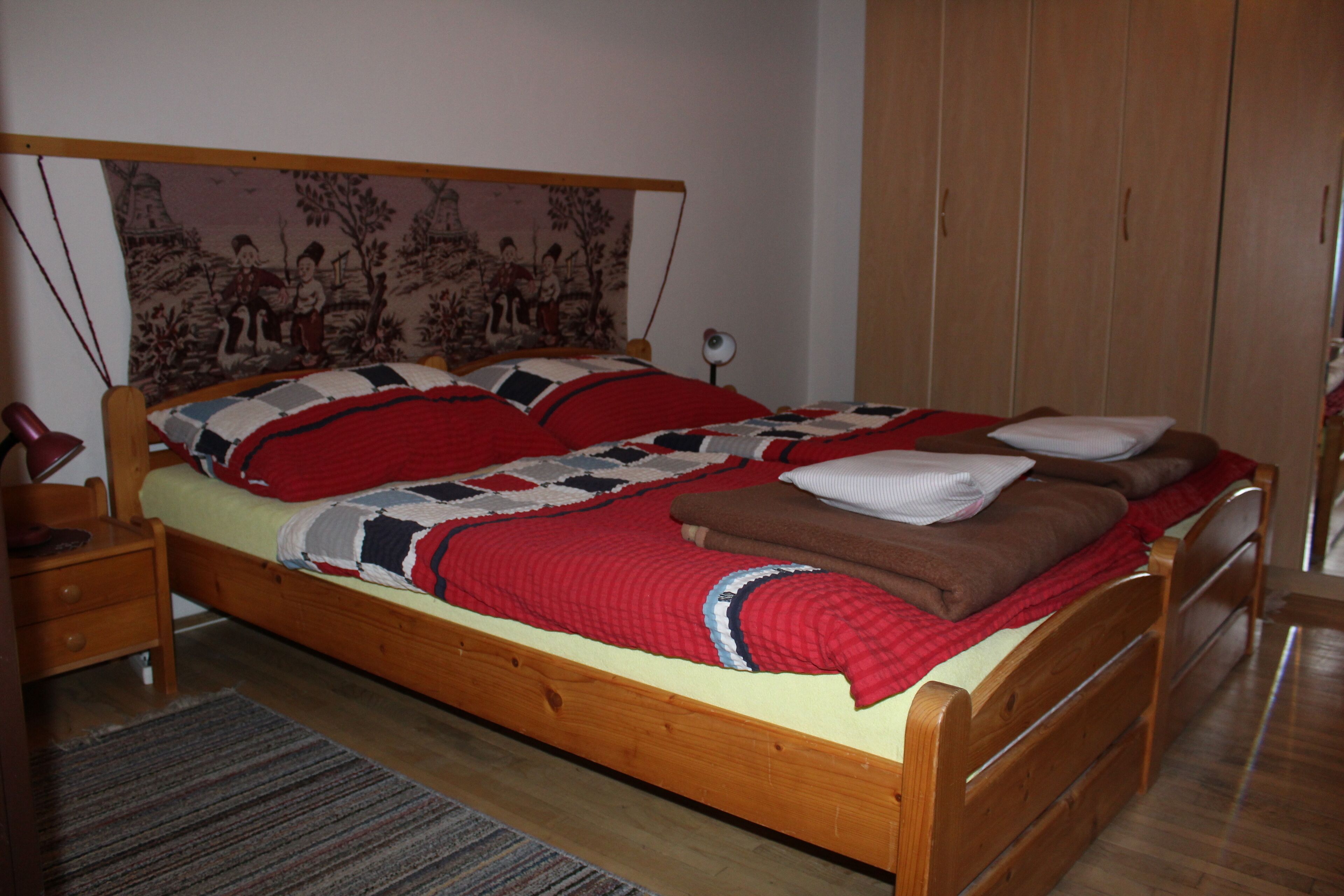 A wooden bed with a quilt, pillows, and a headboard with a tapestry.
