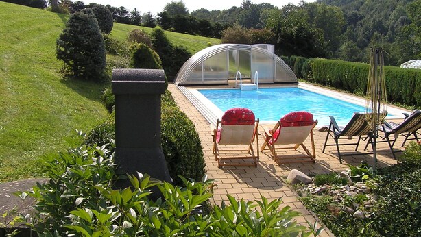 A swimming pool with a glass enclosure, surrounded by a brick patio, and two lounge chairs with red cushions. - Comfortable house in Bohemian Paradise with swimming pool, internet (Turnov)