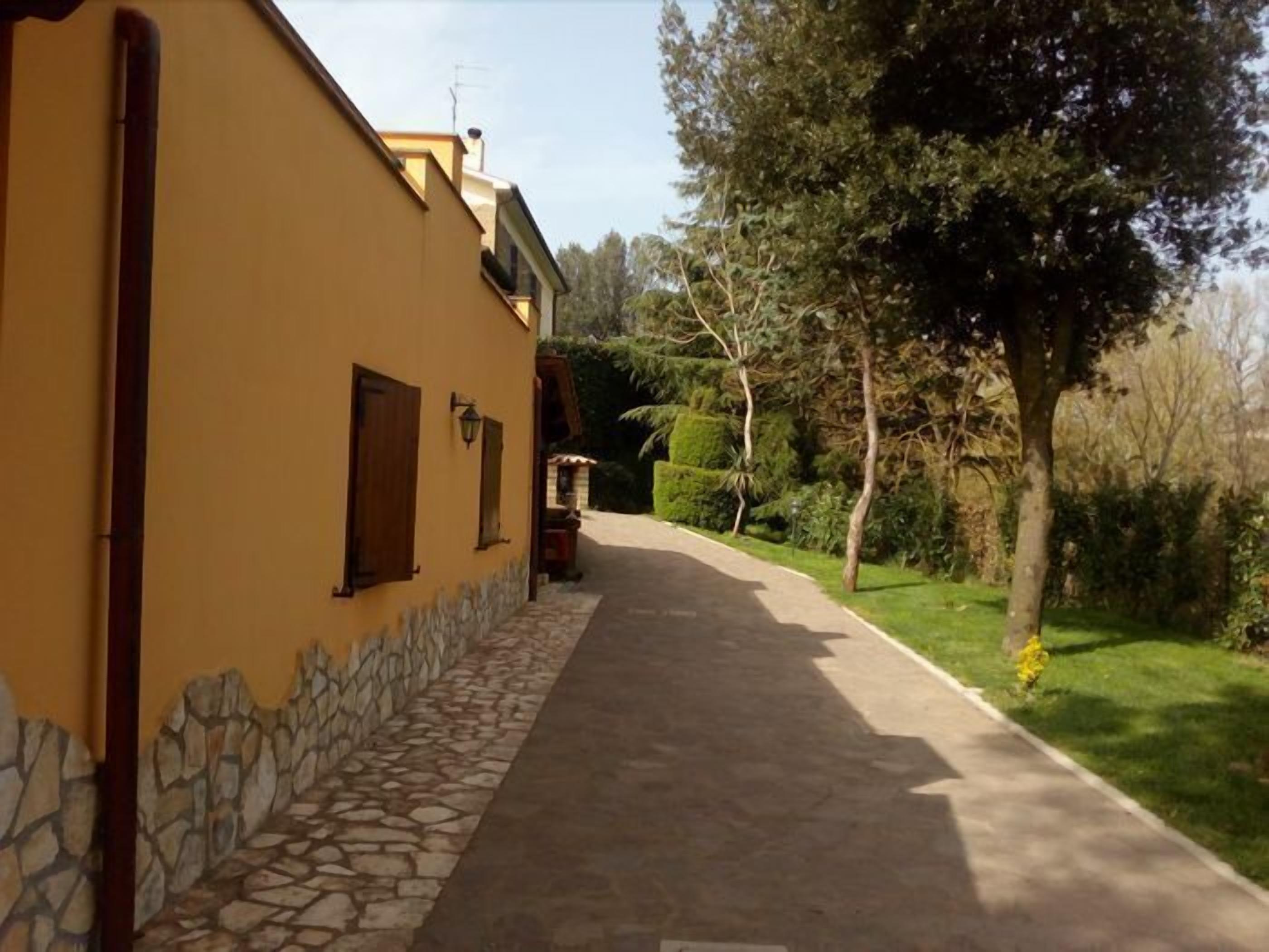 A narrow pathway leading to a yellow building with stone accents and wooden shutters.