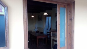 Zona de menjador amb taula i cadires de fusta, un lampadari i una finestra amb cortines.