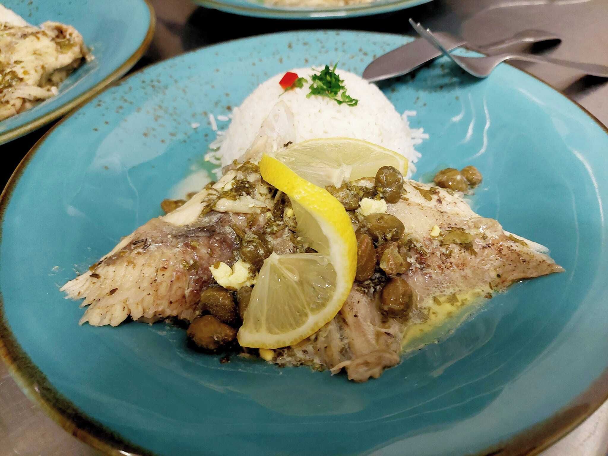 A plate with fish, lemon, capers, and rice.