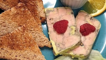 A plate with toasted bread, a slice of meat with raspberries, a small bowl of sauce, and a slice of lemon.