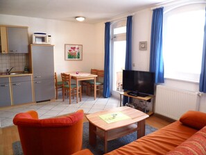 A compact living space with a kitchenette, a dining area, a TV, and a sofa.