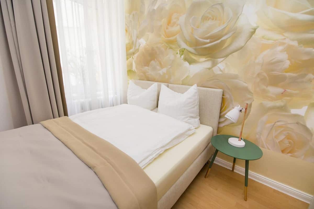 A bedroom with a bed, a nightstand, and a wall with a floral pattern.
