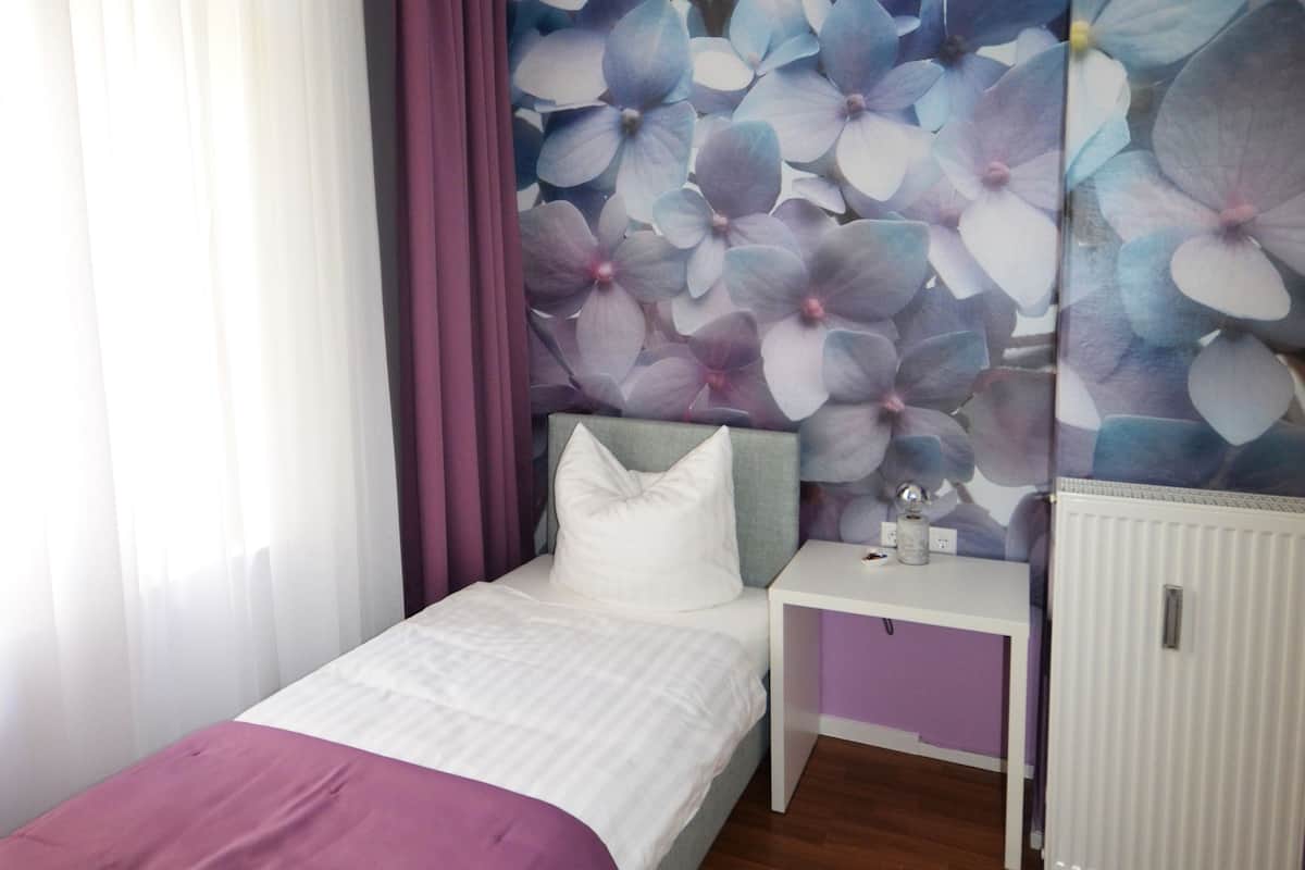 A bedroom with a bed, a nightstand, a radiator, and a wall with a floral mural.