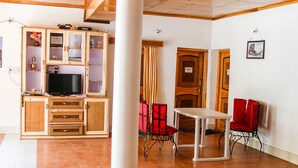 A room with a television, wooden cabinets, a table, and red chairs. - Ibex Guest House (Leh)