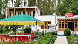 A guest house with a covered outdoor seating area, a pathway leading to the entrance, and a signboard. - Ibex Guest House (Leh)