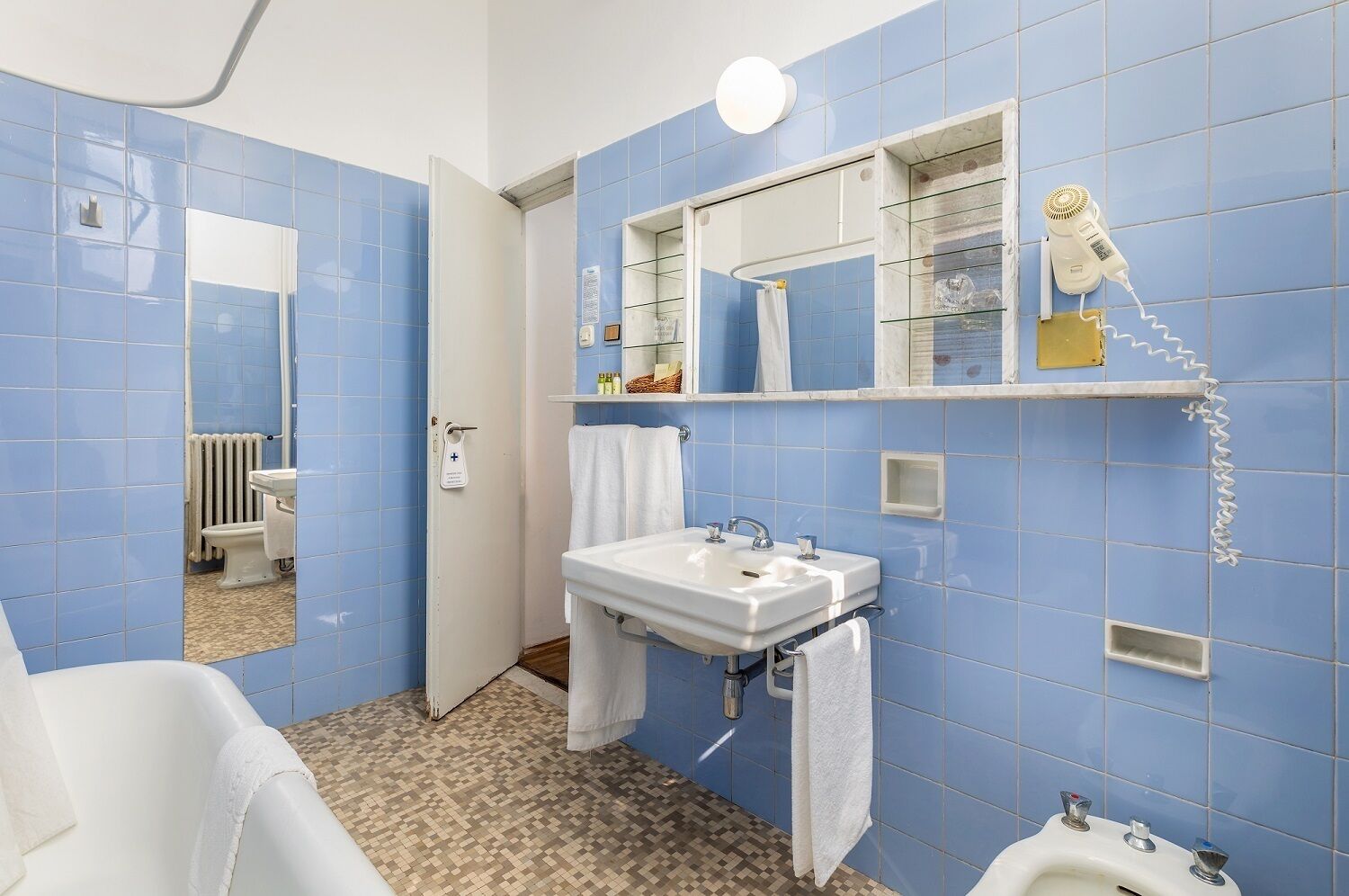 A bathroom with blue tiles, a white sink, a mirror, and a hairdryer on the wall.
