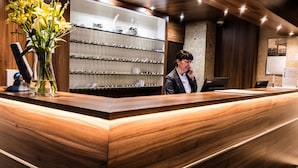 A reception desk with a wooden finish, a vase of yellow flowers, and a display of various glassware. - Brijuni Rooms Karmen (Pula)