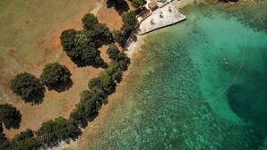 An aerial view of a coastal property with a beach, clear waters, and a small building with a fenced area. - Brijuni Rooms Karmen (Pula)