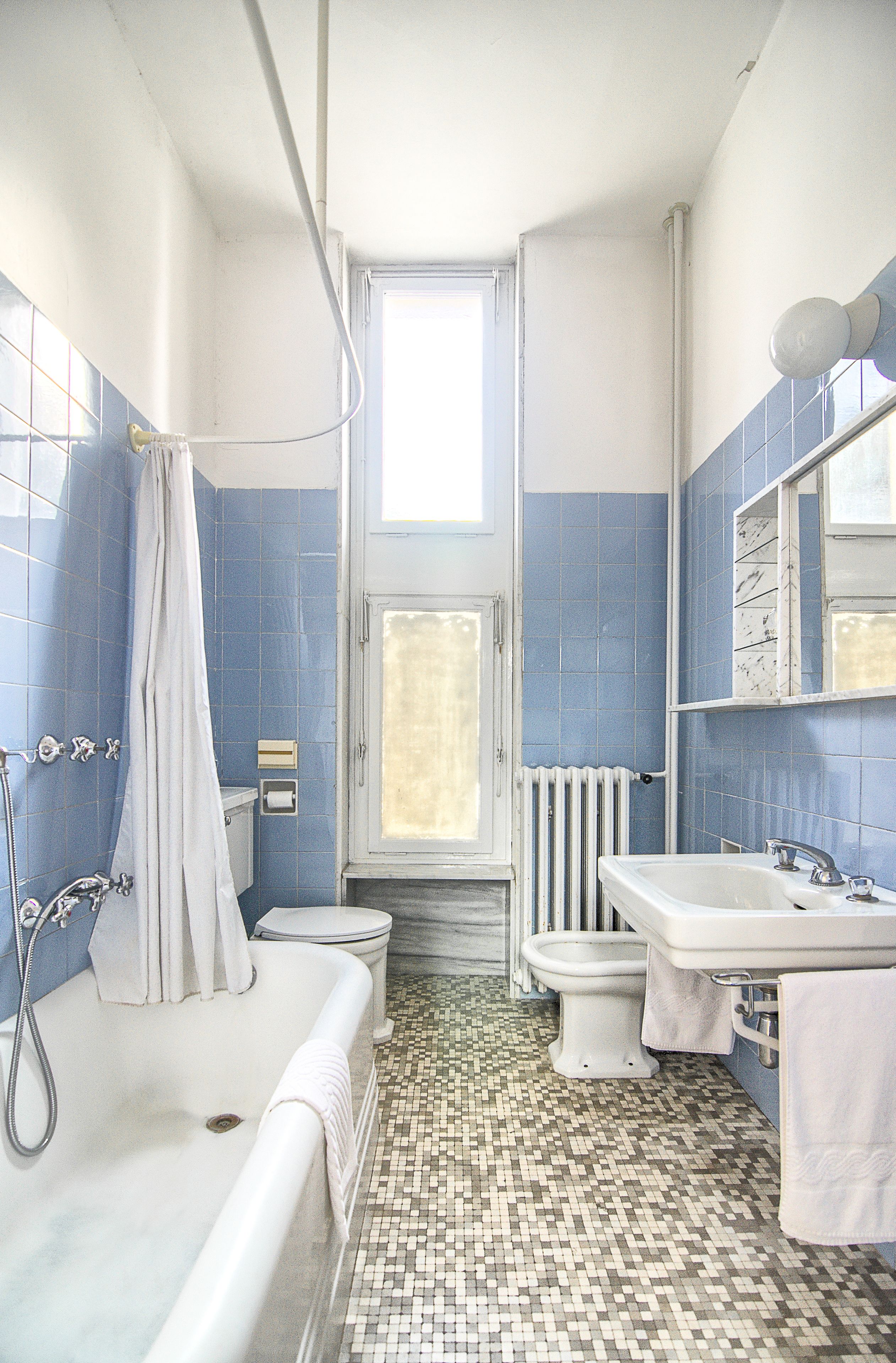 Un baño con bañera, inodoro y lavamanos, con azulejos azules y suelo de baldosas.