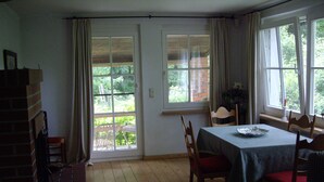 Zona pranzo con tavolo apparecchiato per due, camino in mattoni e ampie finestre con vista sull'esterno.