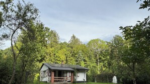 Una piccola casa con un portico, circondata da un prato curato e alberi rigogliosi.