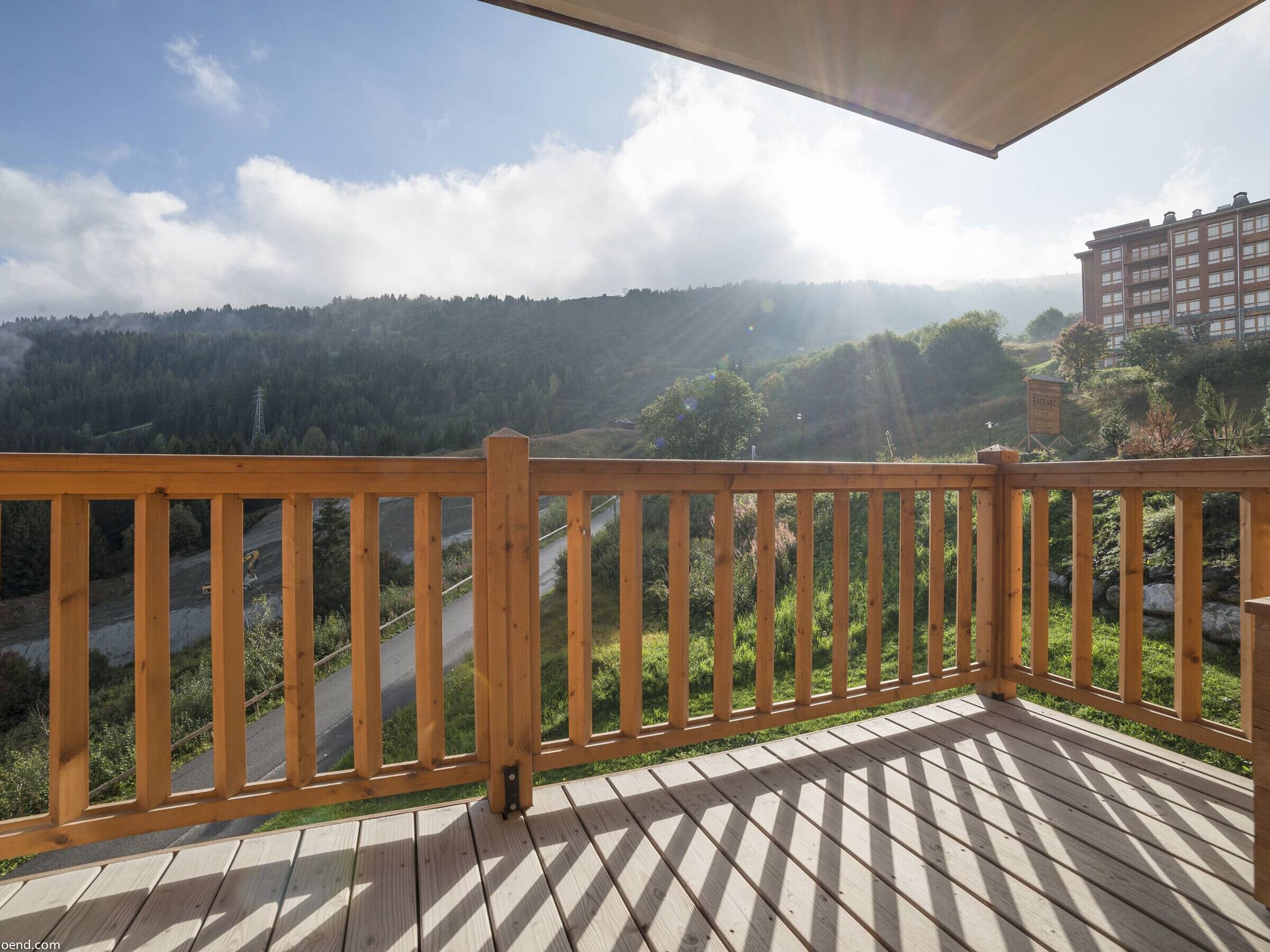 A wooden deck with a view of a forested valley and a building in the background.