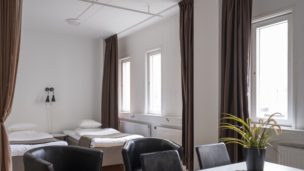 Une chambre d’hôtel avec deux lits, une table à manger avec des chaises, une plante en pot et une fenêtre avec des rideaux.