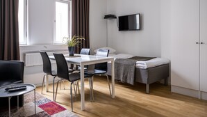 Une chambre d’hôtel moderne équipée d’un lit, d’un bureau avec une chaise, d’un téléviseur fixé au mur et d’une fenêtre avec des rideaux.