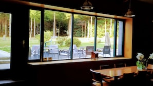 A restaurant with large windows offering a view of an outdoor seating area with chairs and tables. - Casa Garea (Arzua)
