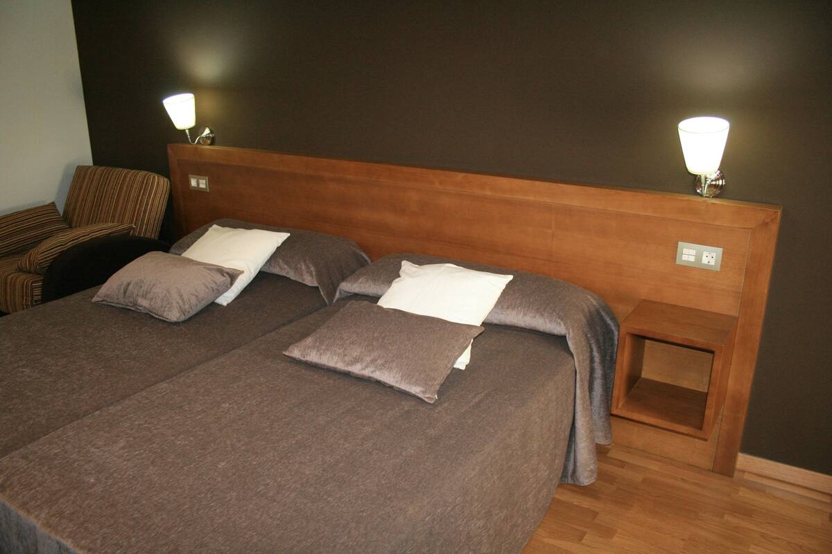 A neatly made bed with a wooden headboard, two bedside tables with lamps, and a striped chair in a hotel room.