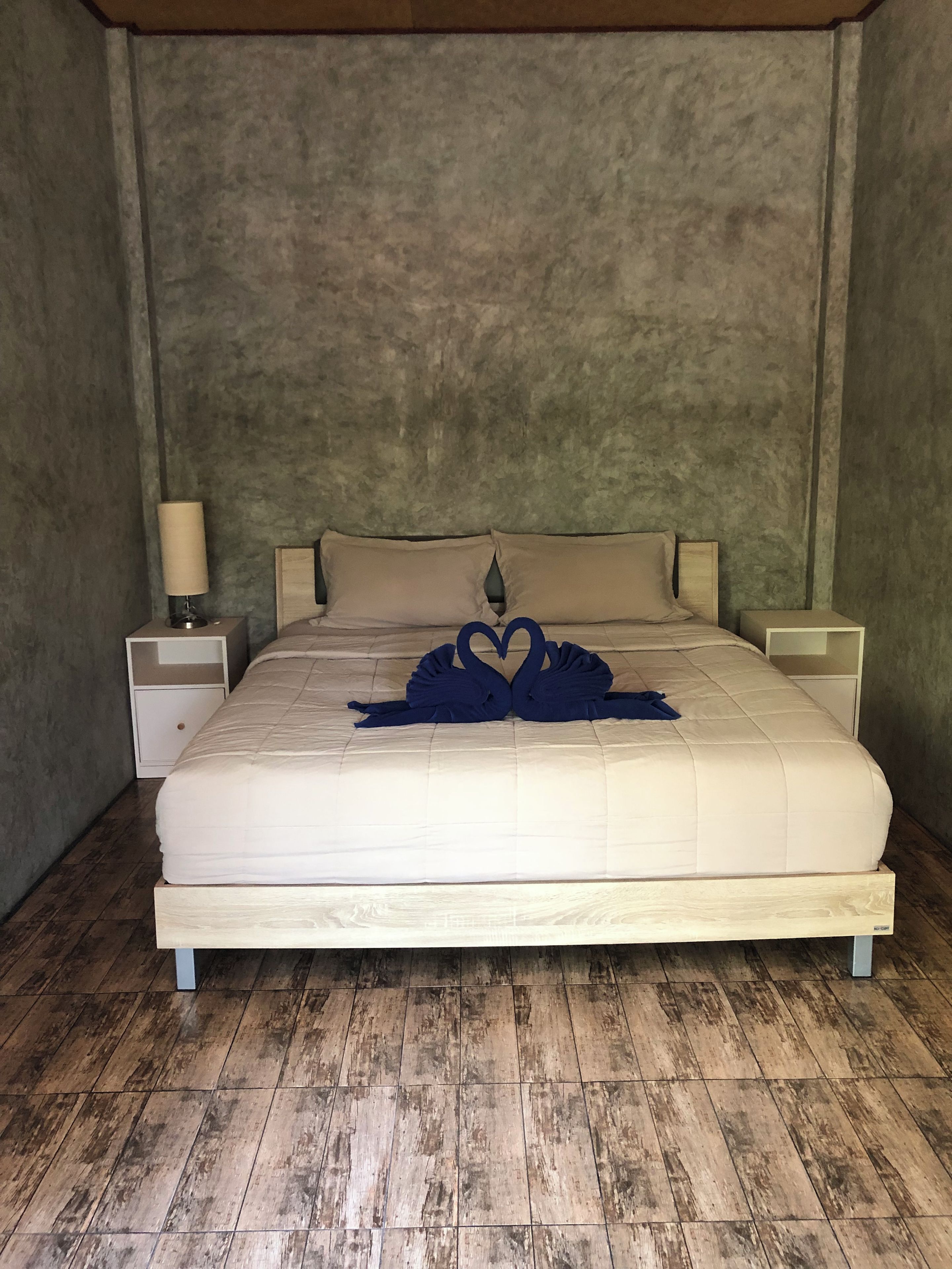 A bedroom with a large bed, two bedside tables, a nightstand, and a wall-mounted lamp.
