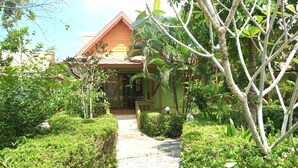 Une maison en bois avec un chemin menant à l’entrée, entourée d’une végétation luxuriante et d’arbres.