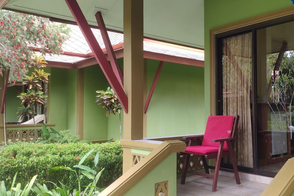 Una habitación con pared verde, una escalera de madera, una silla roja y una silla morada cerca de un ventanal corredera.