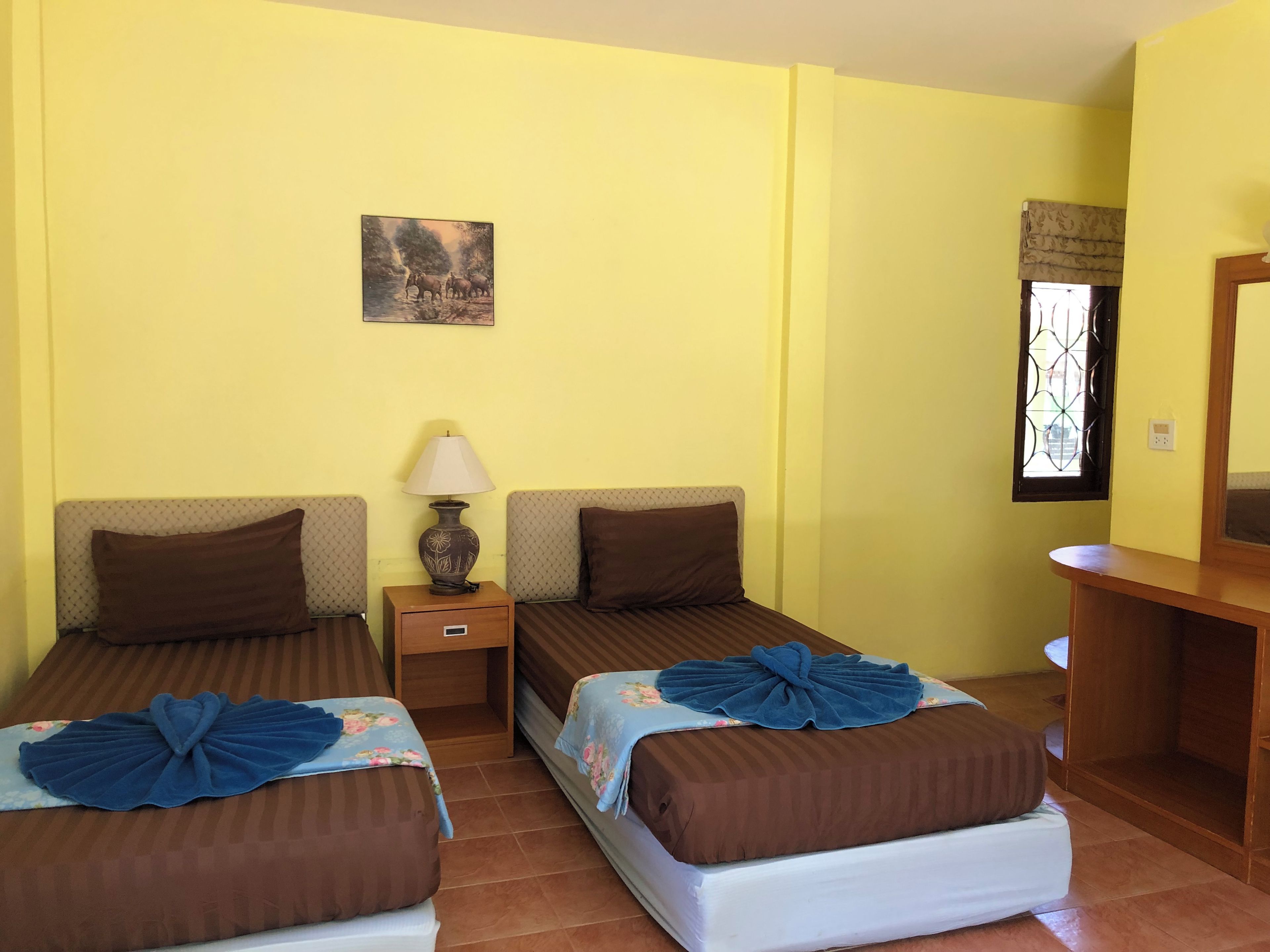 A hotel room with two beds, a nightstand with a lamp, a small table, and a window with a decorative grille.