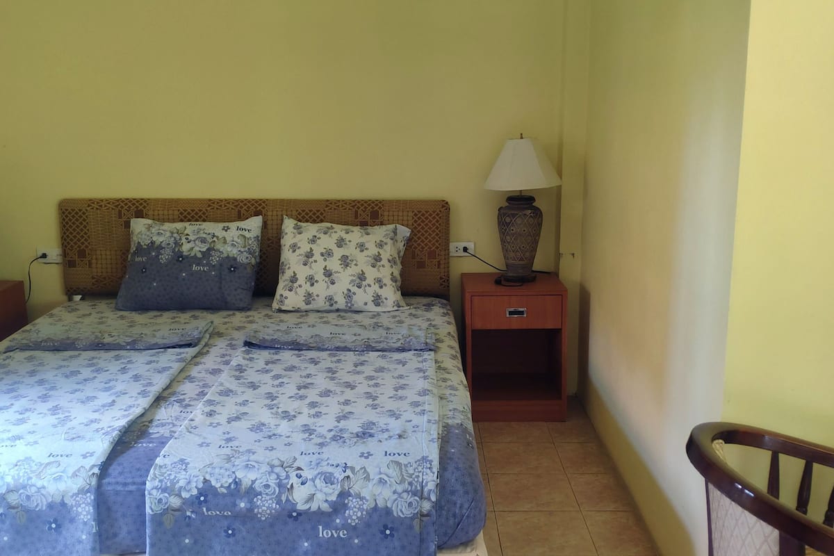 Un dormitorio con cama, dos mesitas de noche, dos lámparas y una silla.
