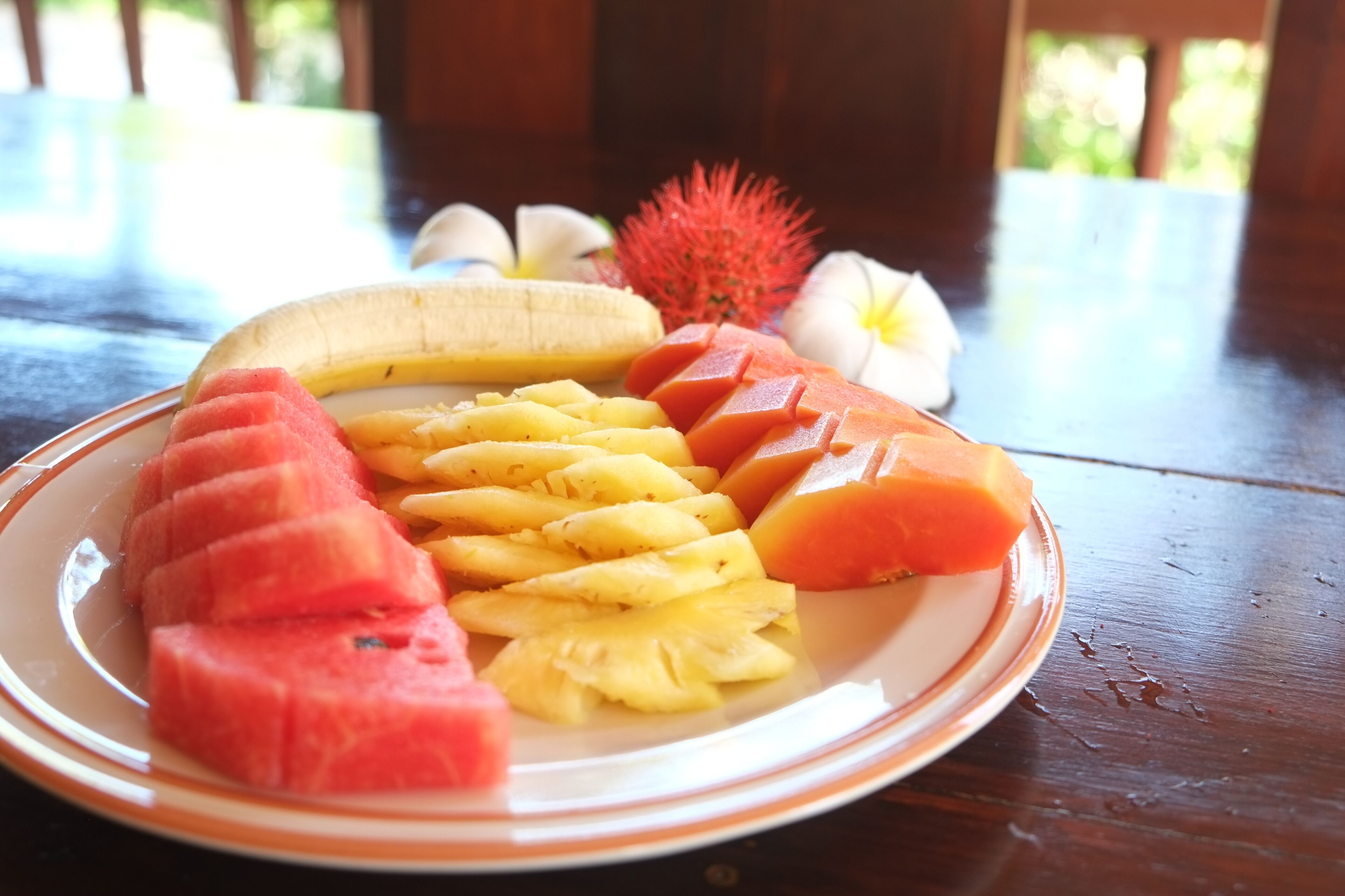 Uma travessa com frutas fatiadas, incluindo melancia, abacaxi e manga, sobre uma mesa de madeira.