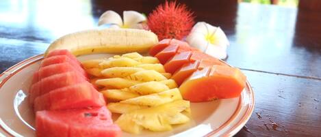 Uma travessa com frutas fatiadas, incluindo melancia, abacaxi e manga, sobre uma mesa de madeira.