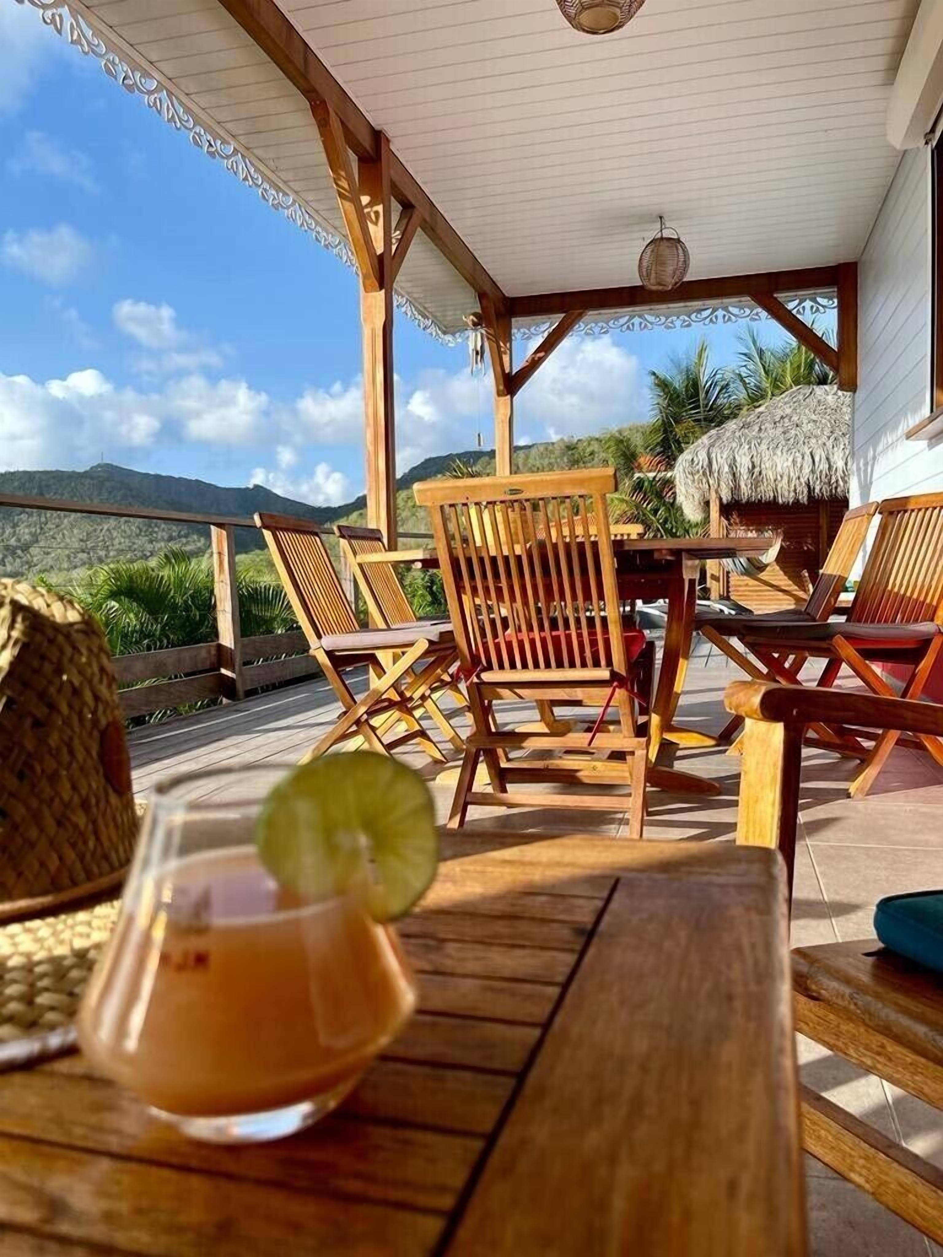 A wooden deck with outdoor seating, a thatched-roof structure, and a view of hills.