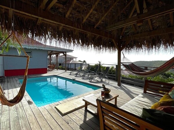 Eine Holzterrasse mit Pool, Liegestühlen und einer Hängematte.
