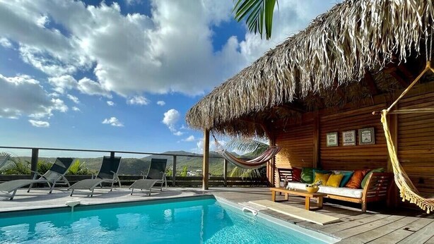 A wooden deck with a pool, lounge chairs, a hammock, and a thatched-roof structure. - New villa with swimming pool, magnificent view of the caribbean sea, 1 'from the beach (Les Anses-d'Arlet)