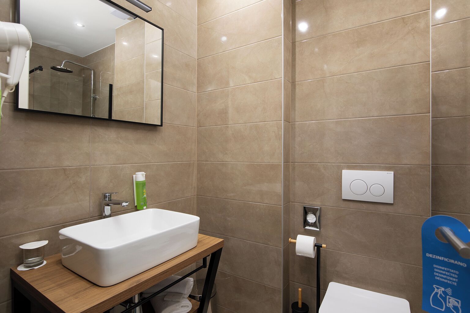 Un baño moderno con un espejo grande, un lavabo blanco, un perchero para toallas y un soporte para papel higiénico.
