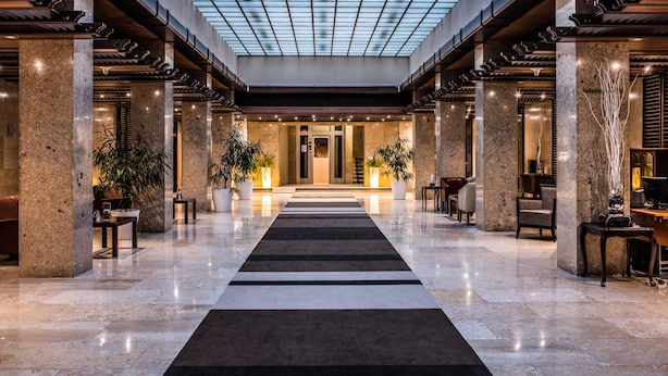A spacious lobby with a central black and white striped carpet, marble columns, and potted plants. - Brijuni Hotel Istra (Pula)