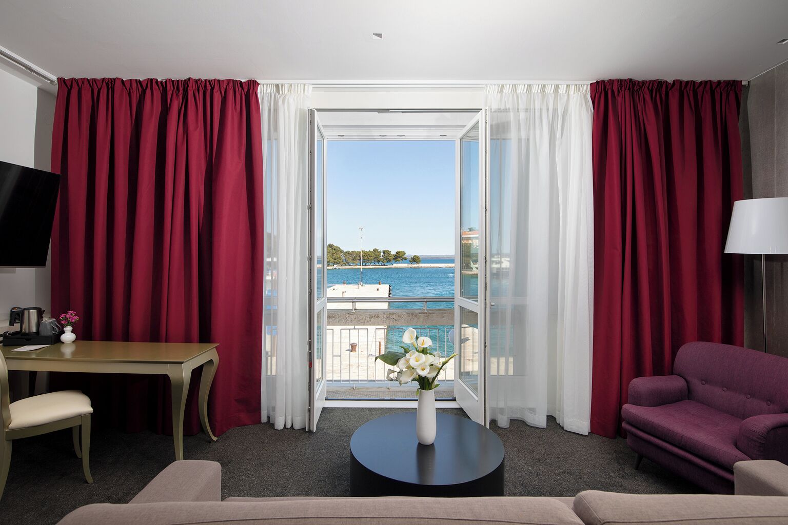 Une chambre d’hôtel avec un balcon, une télévision, une table à manger, un canapé et une table basse.