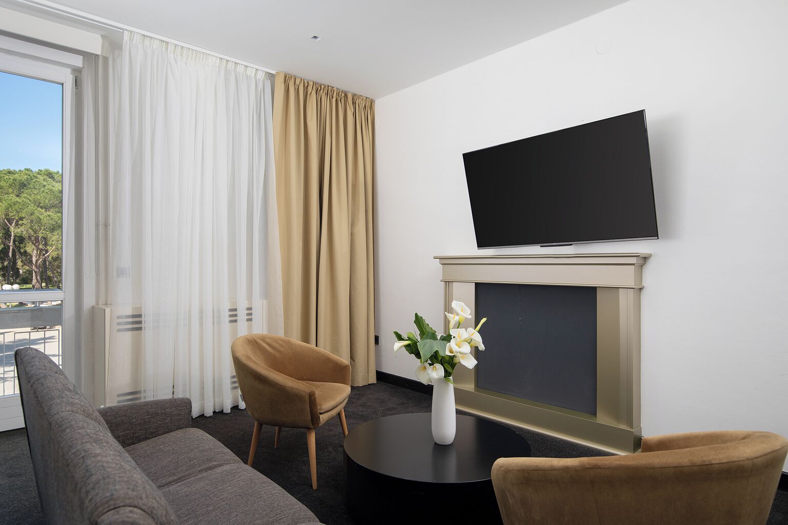 A hotel room with a sofa, two chairs, a flat-screen TV, a fireplace, and a window with curtains.