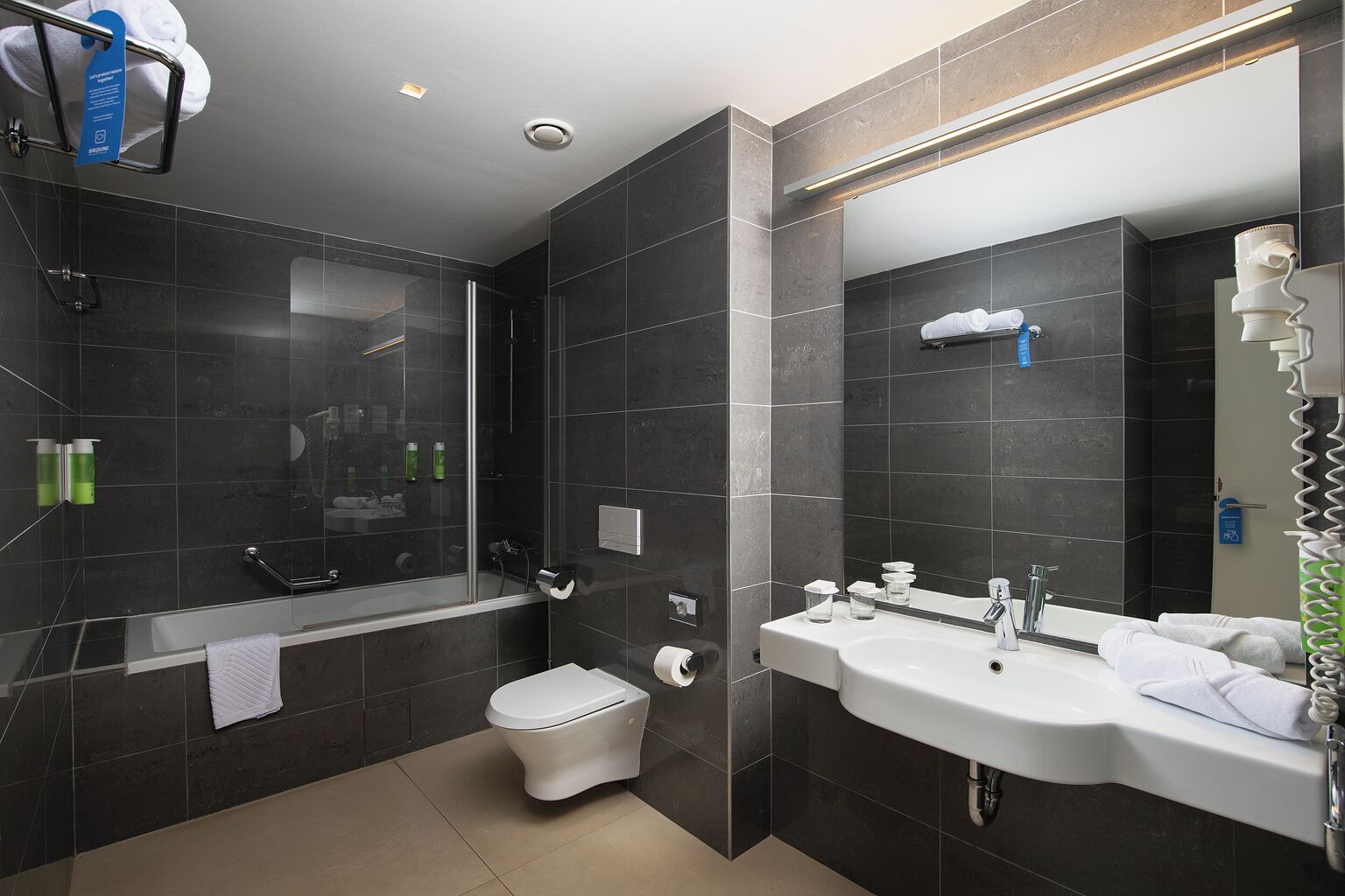 A modern bathroom with a bathtub, toilet, and sink, all with dark tiles.