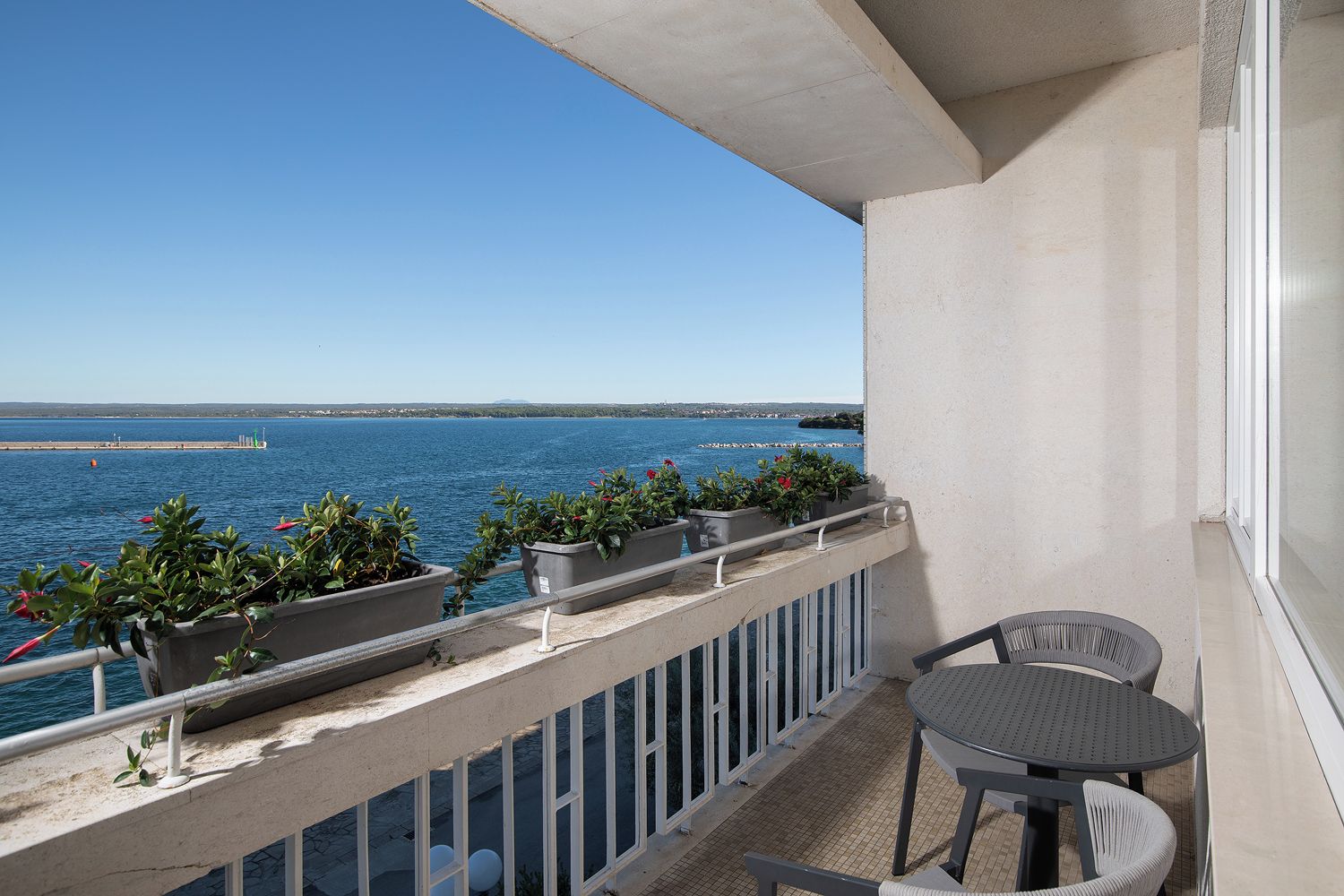 Varanda com vista para o mar, plantas em vasos e mesa com cadeiras.