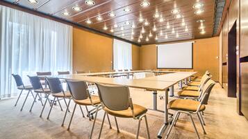 Un salón de conferencias con una mesa larga, varias sillas, una pantalla de proyector y un amplio ventanal con cortinas.