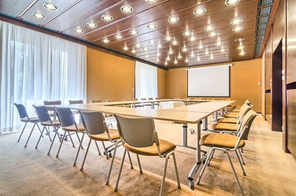 A conference room with a long table, multiple chairs, a projector screen, and a large window with curtains. - Brijuni Hotel Istra (Pula)