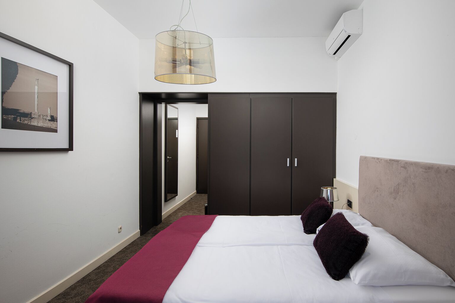 Una habitación de hotel con cama, armario, pasillo y una lámpara colgante.