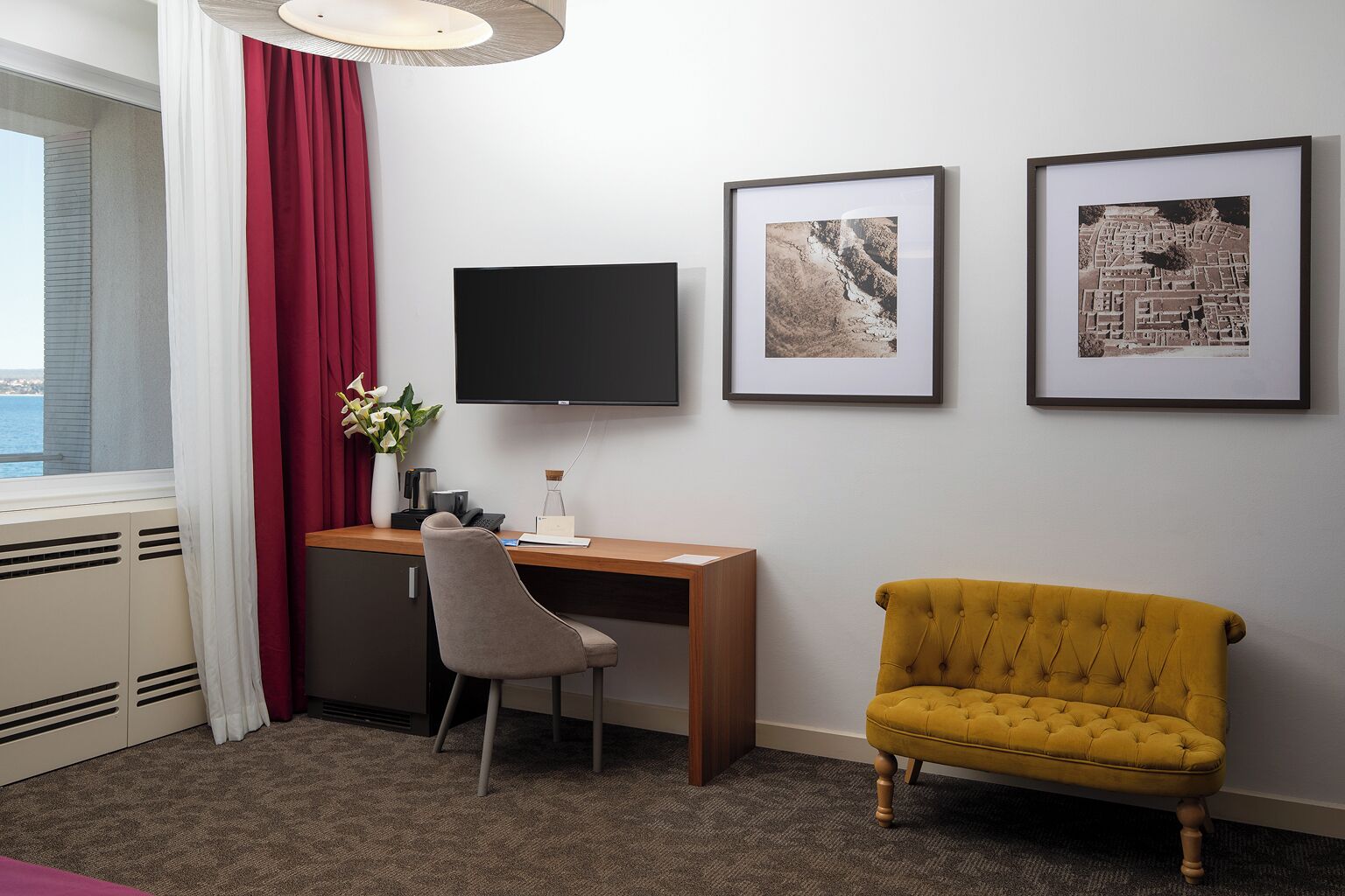 Une chambre d’hôtel équipée d’un bureau, d’une chaise, d’une télévision et de deux tableaux encadrés accrochés au mur.