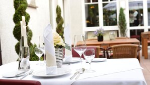 A table set for dining with white tablecloths, silverware, and a vase with a white flower. - Hotel Restaurant Waldesruh (Emstek)