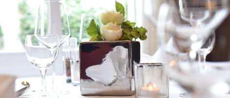 Una mesa dispuesta con copas de vino, una vela y un florero decorativo con flores.