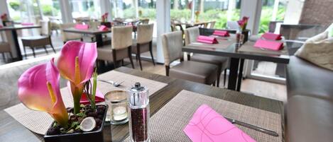 Una mesa de comedor con una planta en maceta, salero y una servilleta rosa.