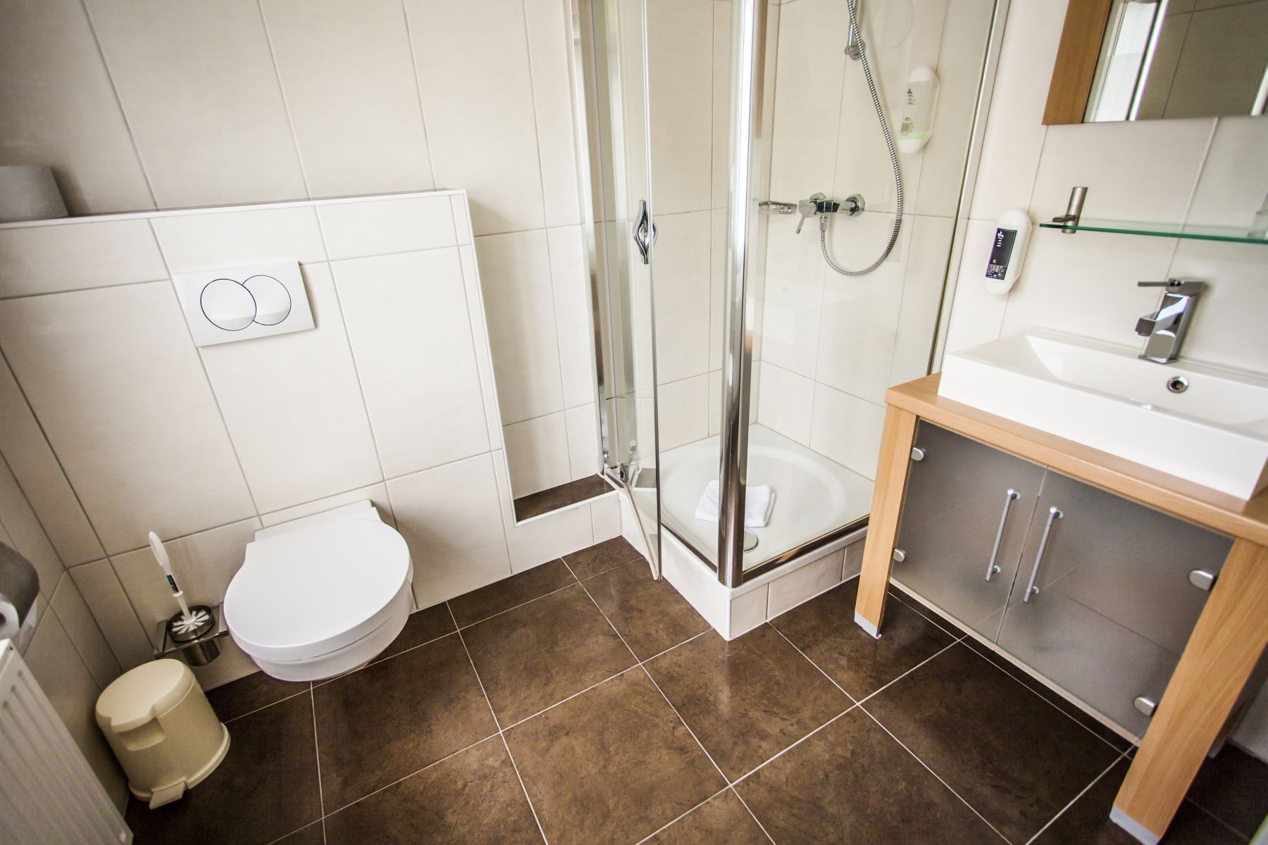 A modern bathroom with a glass-enclosed shower, a white toilet, and a wooden vanity with a sink.